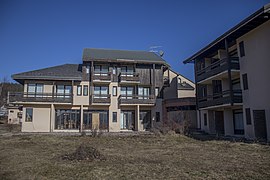 Bâtiment en crépi beige aux balcons en bois, marquant un angle.