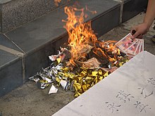 Pilha de dinheiro simbólico pegando fogo; uma mão jogando alguns papéis imitando dinheiro sobre o fogo