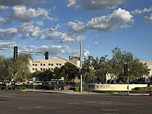 Beyond a street intersection, a hospital complex with five-story and three-story buildings, seen behind a parking lot