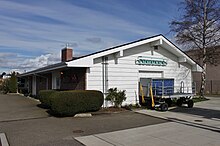 A white building with a low roof and a garage door, blocked by a luggage cart