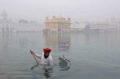 Harmandir Sahib também conhecido como Templo Dourado e seu lago sagrado circundante ("Amrit Sarovar") são visíveis através da neblina em uma manhã fria de inverno. Um voluntário sique realiza a seva ou trabalho limpando o lago sagrado. No siquismo o trabalho é considerado adoração. O Templo Dourado é espiritualmente o santuário mais significativo do siquismo e uma casa de adoração aberta a todas as pessoas, de todas as classes sociais e religiões. Em 1984, a primeira-ministra indiana, Indira Gandhi, enviou o Exército Indiano como parte da Operação Estrela Azul, em um assalto militar ao santuário sagrado, levando à morte mais de mil soldados e civis, além de causar muitos danos ao Templo. O complexo foi reconstruído novamente após os danos de 1984. Ele é um conjunto de edifícios ao redor do santuário e do lago artificial. O complexo do Templo Dourado foi nomeado Patrimônio Mundial da UNESCO e sua aplicação está pendente na lista provisória da UNESCO. (definição 4 263 × 2 800)