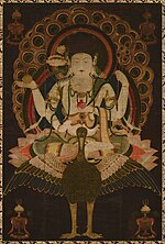 Frontal view of a deity with four arms seated on a bird in lotus position embellished with ornaments.