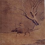 A boy riding an ox and a tree.