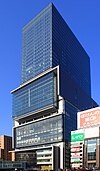 Ground-level view of a blue, glass high-rise; it is divided into three distinct sections along its height