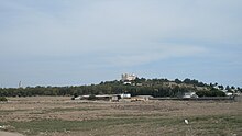 Vue d'une plaine avec au fond une colline avec un grand édifice religieux et sur la gauche un minaret à l'arrière-plan.