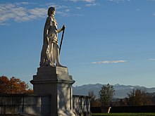 Photographie en couleurs représentant la statue en pied d'un personnage regardant une chaîne de montagnes au loin.