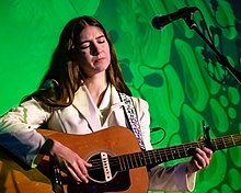 Weyes Blood playing guitar at a microphone