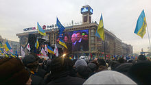 Desítky modrých a žlutých ukrajinských vlajek jsou drženy nahoře v širokém davu, který sleduje velkoplošné obrazovky na čtvercové budově.
