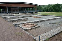 Ruines de bâtiments devant un bâtiment moderne en bois et en métal.