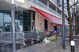 Vue du restaurant Events fermé entouré de barrières métalliques avec des dépôts de gerbes de fleurs.