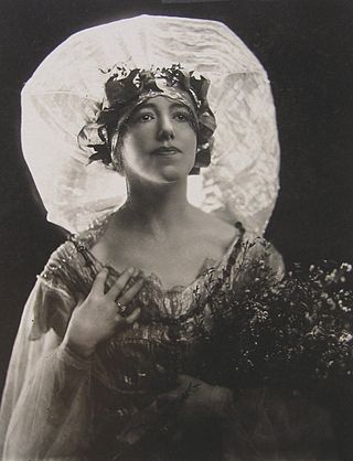 Photographie en noir et blanc d'une femme blanche en buste de trois quarts vers la droite sur fond noir. La femme regarde vers le coin supérieur droit et porte un déguisement ample et sylvestre.