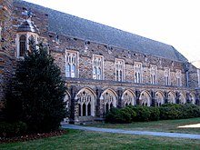 A Gothic-style exterior showcases Cathedral-like windows with the intricate framework and dark, colorful stone, with bushes and grass in the foreground