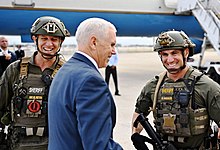 Far-right conspiracy theories such as QAnon are widely accepted among Trump supporters with half believing both elements of the theory according to polling data from 2020. Pictured are Vice President Mike Pence and members of the Broward County, Florida SWAT team assigned to a high-profile security detail, one of whom is wearing a QAnon patch. Pence posing with QAnon police crop.jpg