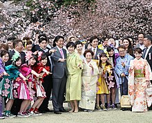 Shinzo Abe and Akie Abe standing in Shinjuku Gyoen under cherry blossom trees, pointing at the distance