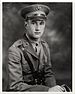 Head and torso of a white man sitting with his right arm resting on something in front of him. He is wearing a military uniform with a wide belt, a strap diagonally across the chest, and a peaked cap.