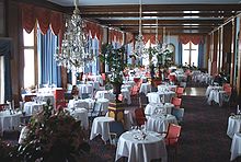 Salle à manger d'un restaurant gastronomique avec des tables rondes nappées, lustres en cristal et plantes d'intérieur