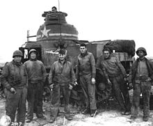 photographie en noir et blanc montrant six hommes posant debout devant un char, avec un septième dans la tourelle