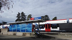 White train pulled up at platform; the platform has a shelter