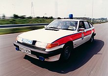 A large white car with a red stripe on the side moving along highway