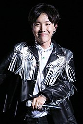 J-Hope dancing against a black sky. A mic is in his right hand.