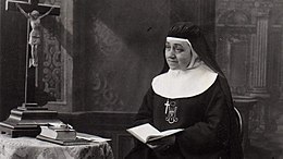 Photo noir et blanc d'une religieuse, un livre en main, près d'un crucifix