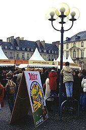 Photographie d'une place de Rennes pendant la "Fête d'Astérix et Obélix". De nombreuses personnes ainsi que des tentes pour les stands et un panneau "Astérix" sont visibles. Notons, sur le panneau, l'inscription "Les marchés de Condate".