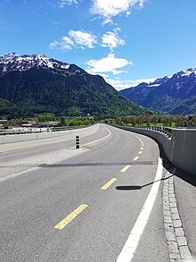 Blick auf die Fahrbahn des Goldswil-Viadukts (eine lange Gerade), an einem sonnigen, frühlingshaften Tag. Im Hintergrund eine leicht mit Schnee bedeckte Bergkette