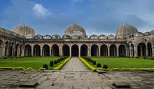 A view of a mosque with three domes and multiple entrance halls with a garden in the foreground