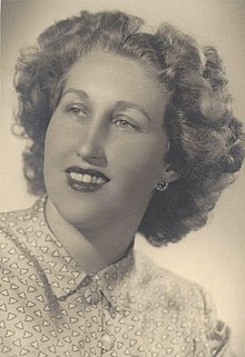 B&W portrait photograph of a smiling woman with curly blonde hair, wearing a buttoned-up collared-blouse