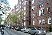 Vue d'une rue avec plusieurs voitures garées le long de façades d'immeubles identiques.