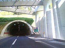 Tunnel portal, variable traffic signs indicating traffic flow direction are visible at the tunnel entrance, as well as tunnel portal cover and concrete columns supporting the cover