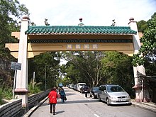 Cars parked on one-side of a tree-lined street with pedestrians walking under an archway which crosses the street