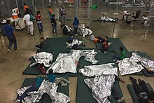 Children and juveniles in a wire mesh compartment, showing sleeping mats and thermal blankets on floor