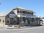 Double-story building with hipped roof. 3 bays, symmetrical. Double verandah, plain roof, returned, with plenty of ornamental cast-iron detail. Hoods and keystones above windows. Front door 6 panels, leaded fanlight, stained glass. Sliding sash windows. Multicoloured front door. Built in 1839 for Dr James Christie, first full-time government doctor in the area. He was also town councillor, MP & director of Beaufort Bank. The building served as a police station 1898 till after the Anglo-Boer War. Type of site: House Current use: Backpackers.