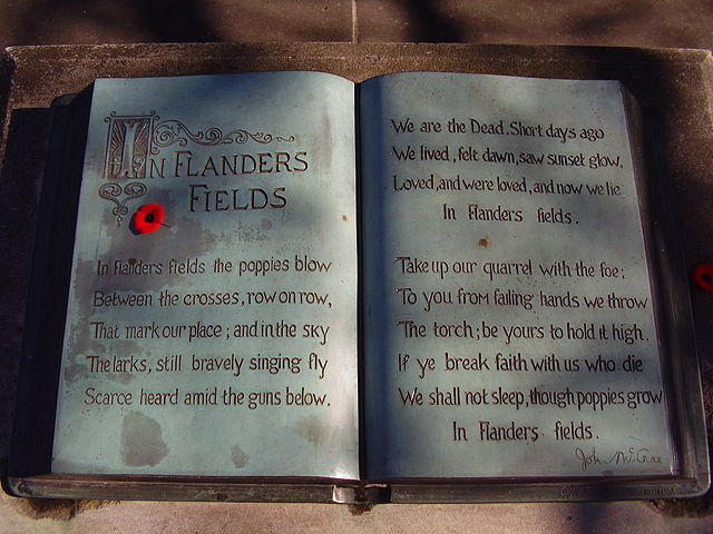 A sculpture in the form of an open book. The text of the poem "In Flanders Fields" is written within and a small red poppy lies on top.
