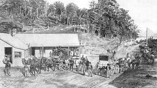 A road in the right half, with several horse drawn coaches and passengers in front of the Bealey Hotel (on the left-had side). Behind the hotel is cleared ground with fences and then bush and trees.