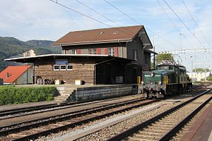 Green locomotive in front of two-story building with gabled roof