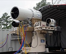 Members of the Directed Energy and Electric Weapon Systems Program Office of the US Navy, fire a laser through a beam director on a Kineto Tracking Mount, controlled by a MK-15 Phalanx Close-In Weapons System US Navy 100119-N-0365D-001 Members of the Directed Energy and Electric Weapon Systems Program Office fire a laser through a beam director on a Kineto Tracking Mount, controlled by a MK-15 Phalanx Close-In Weapons System.jpg