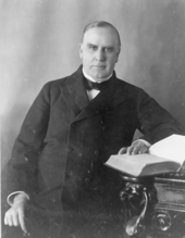 McKinley assis à un bureau devant un livre ouvert.