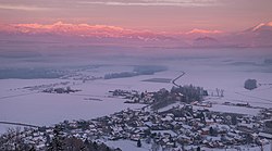 Snow-covered rural town with fields nearby and forests and mountains in the distance