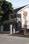 A double storey dwelling with some of the original stone construction exposed on the side of the house. The building has notable veranda trellising and the original character is maintained except for the roof replacement. Architectural style: Regency townhouse. Type of site: House.