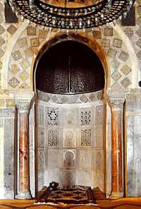 Vue centrée sur le mihrab de la Grande Mosquée de Kairouan, dont l’état actuel date de la période aghlabide (neuvième siècle). Il s’agit d’une niche soigneusement décorée, aménagée à peu près au milieu du mur méridional, dit de la qibla, de la salle de prière.