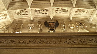Relieve na sala capitular baxa. Escudu de Carlos V flanqueado por Hércules y Xuliu César. A un llau atópase la cruz de Borgoña y al otru les columnes de Hércules.