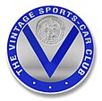 Logo du "Vintage Sports-Car Club" (club anglais de sport auto réservé aux voitures d'avant 1940). Le V de Vintage est surmonté d'un bas relief représentant Saint Christophe portant l'enfant Jésus et la phrase en français "Regarde Saint Christophe puis va-t-en rassuré".