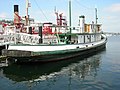 Photograph of the tug Arthur Foss at dock on Lake Union as a museum ship, white with green trim, showing the stern and a view across the lake.