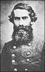Old photo shows a frowning man wearing a double-breasted gray military uniform. He sports a beard so large that it hides the entire lower part of his face.