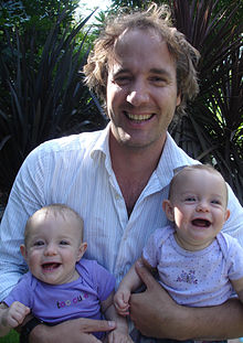 A photo of a smiling Billy Bob Buttons holding two very young children, one in each arm.