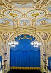 A theatre audltorium with gold, decorative walls and ceiling, and blue stage curtain.