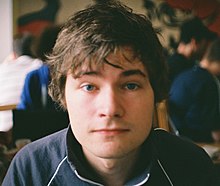 A front-facing image of the face of a 21-year old German man with brown hair and wearing a blue jacket