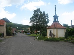 Náves v Kololeči, v pozadí hrad Košťálov